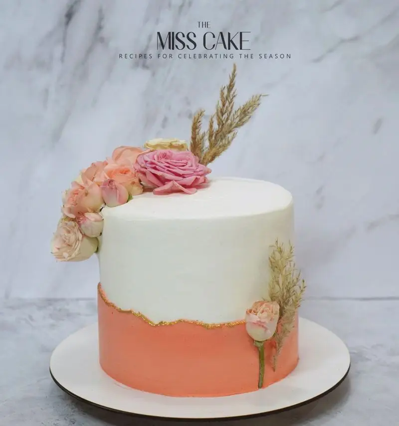 کیک سفارشی میس کیک برای تولد و جشن‌ها، با طراحی مدرن دو رنگ سفید و هلویی، تزیین گل‌های طبیعی و خط طلایی.