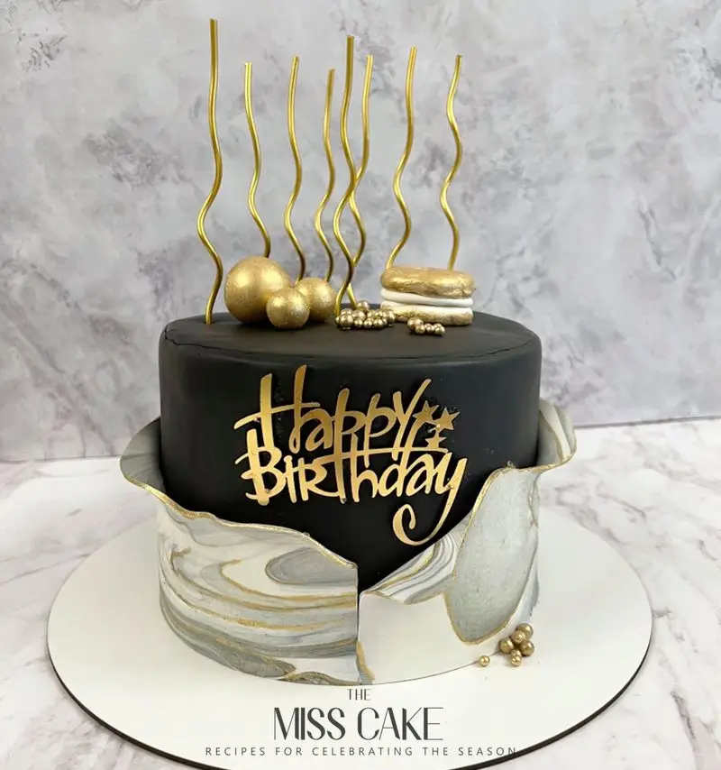 کیک تولد دو طبقه مشکی و طلایی شیک از میس کیک، با دیزاین خاص مرمر و تزیینات لاکچری. بهترین انتخاب برای جشن‌های شما.
