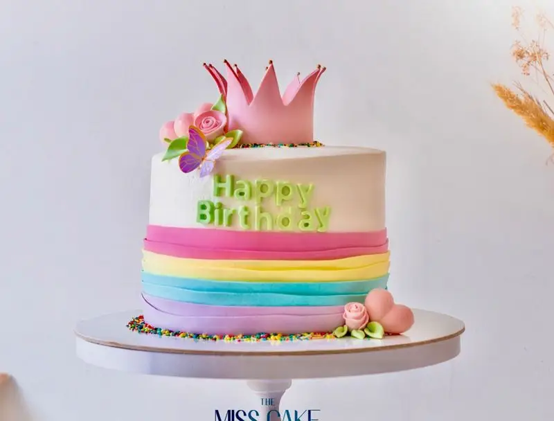 کیک تولد زیبای میس کیک با تم شاهزاده خانم، تاج صورتی، پروانه و نوارهای رنگین کمان. بهترین گزینه برای سفارش کیک‌های خاص و جشن‌ها.