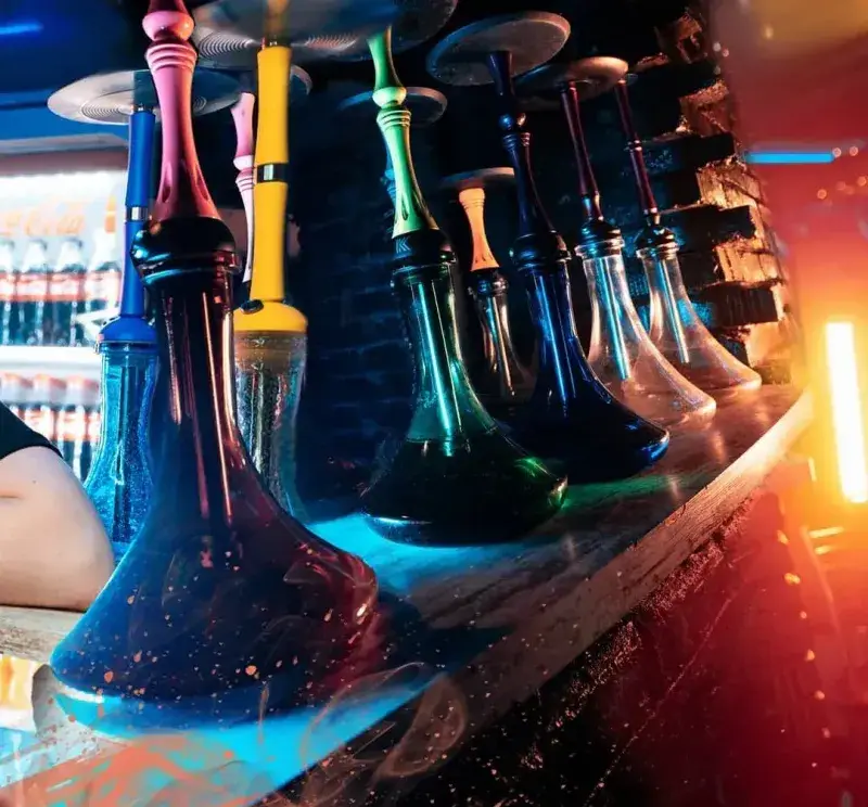 قلیان‌های شیک و رنگارنگ روی میز چوبی در دکوراسیون خاص سفره خانه و کافه قلیان کریمخان با نورپردازی زیبا.