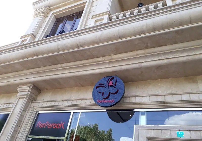 تصویر نمای بیرونی فروشگاه پیتزا پرپروک با معماری سنگی کلاسیک و تابلوی گرد آبی رنگ حاوی لوگوی برجسته و نام PerPerook.