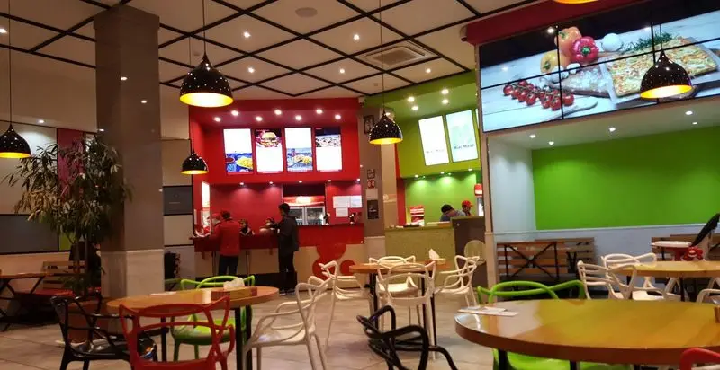 فضای داخلی مدرن و رنگارنگ رستوران پیتزا پرپروک با میز و صندلی‌های شیک، منوهای دیجیتال روشن و کارکنان آماده سرویس‌دهی به مشتریان.