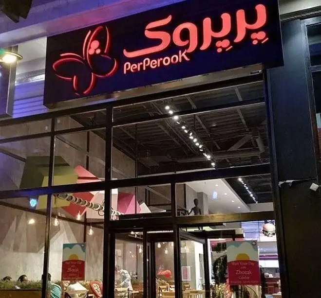 تصویری از نمای شبانه رستوران پیتزا پرپروک، با تابلوی روشن و لوگوی پروانه، فضای داخلی شیک و مدرن را نشان می‌دهد.