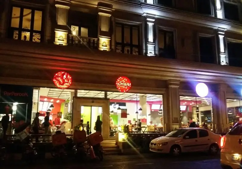 نمای بیرونی رستوران فست فود پیتزا پرپروک در شب با تابلوهای درخشان و موتورسیکلت‌های آماده تحویل غذا در خیابان.