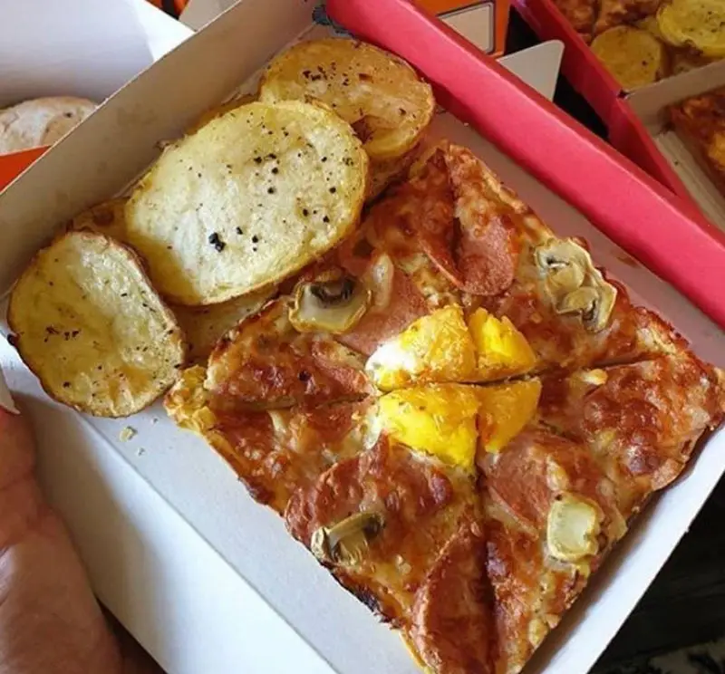 پیتزا خوشمزه پرپروک با سوسیس، قارچ و تکه‌های تخم‌مرغ به همراه سیب‌زمینی‌های حلقه‌ای تنوری در بسته‌بندی بیرون‌بر، ایده‌آل برای یک وعده غذایی کامل و سفارش آنلاین.