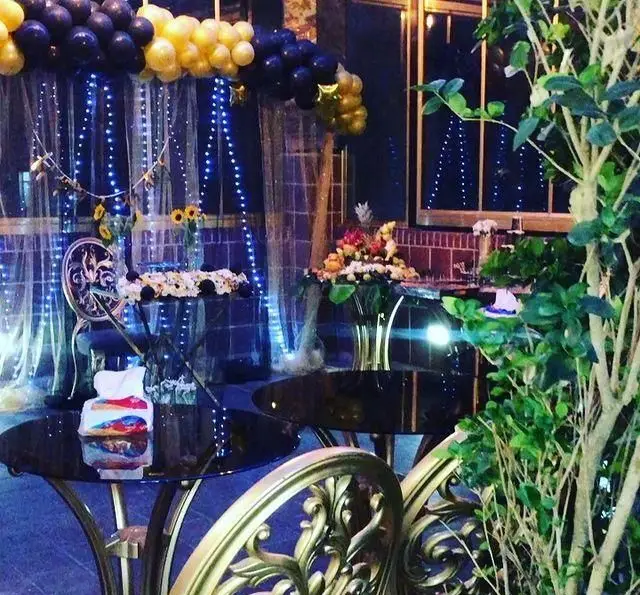 فضای رمانتیک و دکوراسیون خاص کافه رستوران عمارت برای جشن‌ها. بادکنک‌آرایی آبی-طلایی، نورپردازی شب و میزهای شیک در فضای باز.