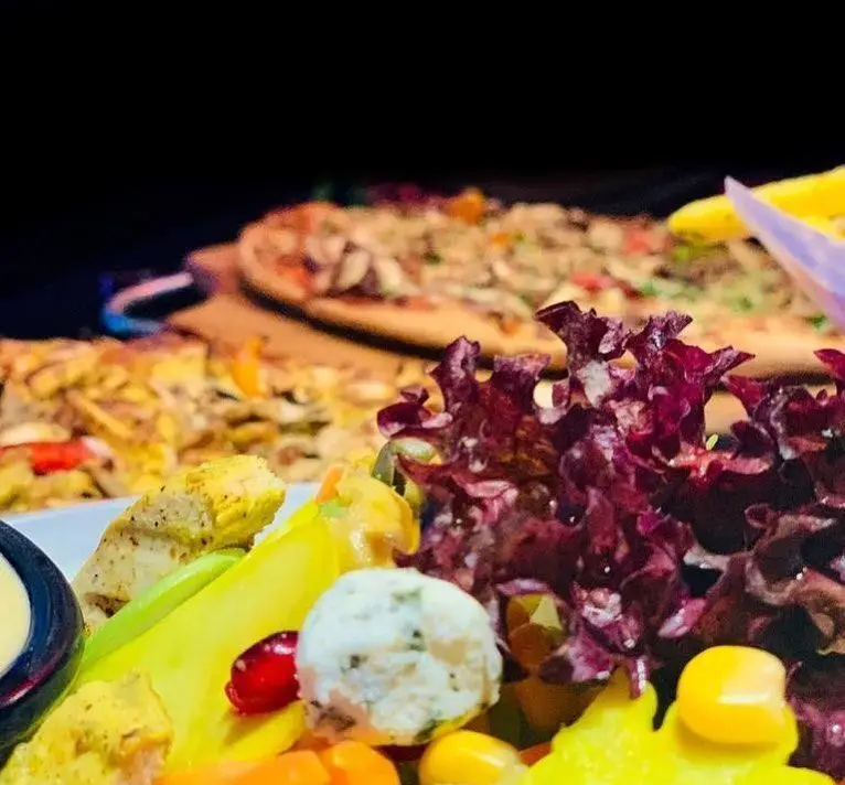 تصویری از میز غذای متنوع پیتزا شب شامل پیتزاهای خوشمزه و سالاد تازه با مرغ گریل شده، کاهو قرمز، ذرت و سس. انتخابی لذیذ و سالم.