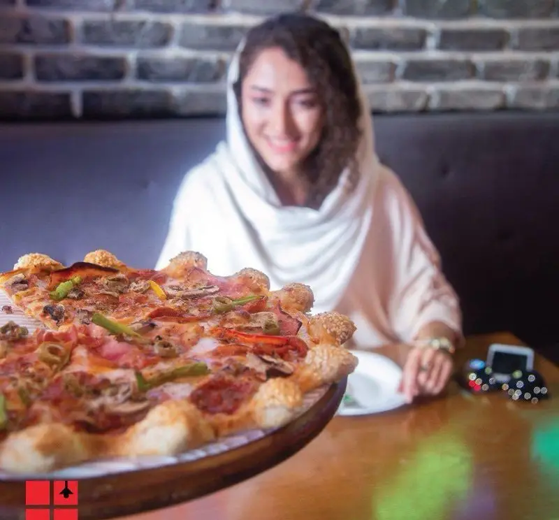 مشتری خوشحال در رستوران پیتزا شب، در حال تماشای پیتزای خوشمزه و خاص با کراست کنجدی و مواد تازه. تجربه یک غذای لذیذ.