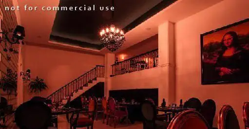 فضای داخلی شیک و دلنشین کافی شاپ پارادیزو با میز و صندلی های چیده شده، راه پله، لوستر زیبا و نقاشی مونالیزا.