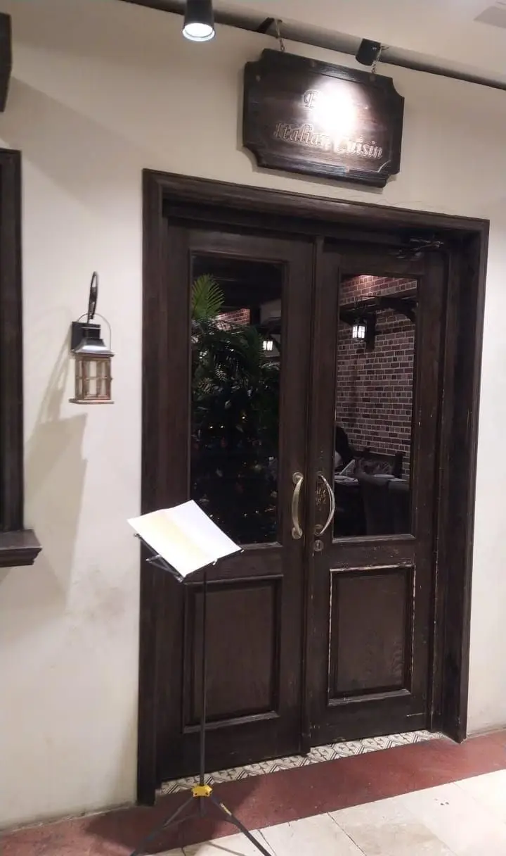 نمای بیرونی و ورودی رستوران ایتالیایی پارلا، شامل درب‌های چوبی، تابلوی منقوش "Italian Cuisine" و منوی روی استند.