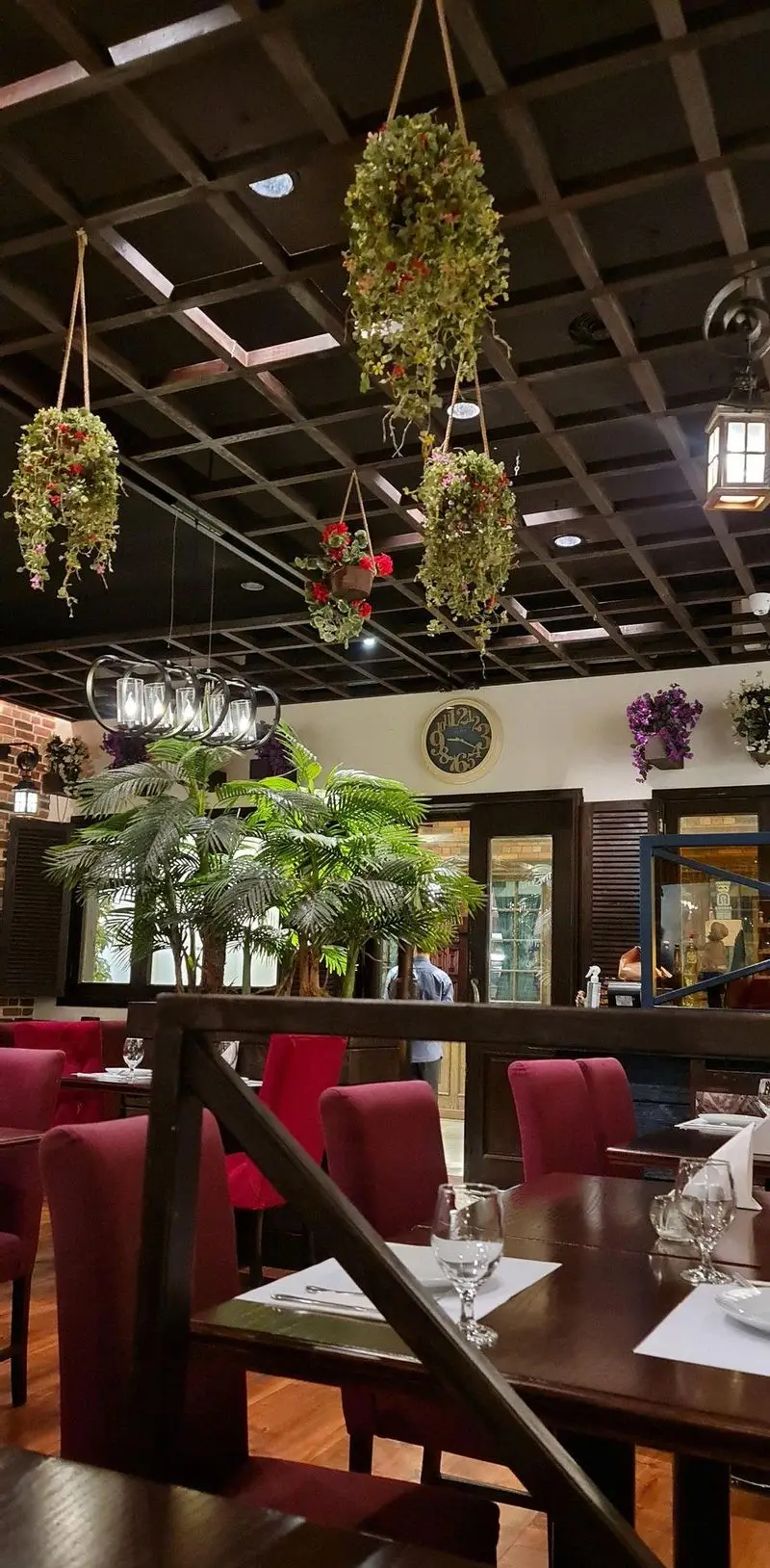 تصویر دکوراسیون داخلی رستوران ایتالیایی پارلا با سقف چوبی تیره، گلدان‌های آویز، میزهای چوبی شیک و صندلی‌های قرمز راحت.