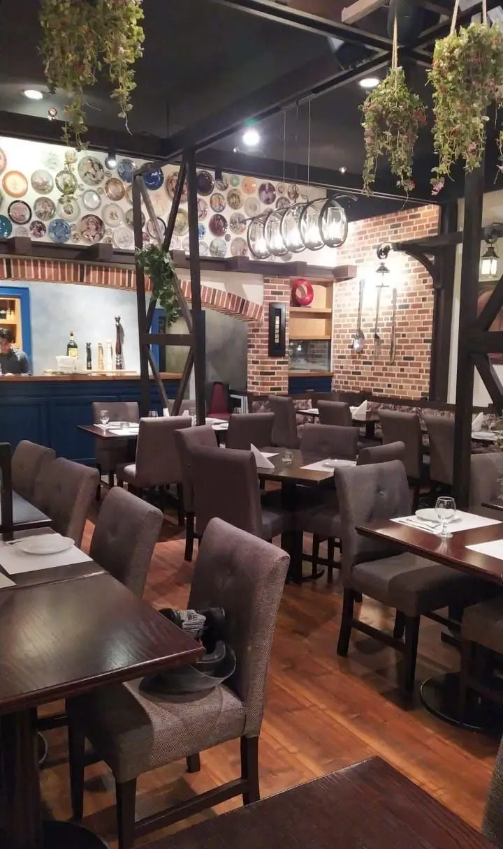 فضای داخلی رستوران ایتالیایی پارلا با دکوراسیون گرم و دلنشین، میز و صندلی‌های شیک، دیوار آجری و بشقاب‌های تزئینی خاص.