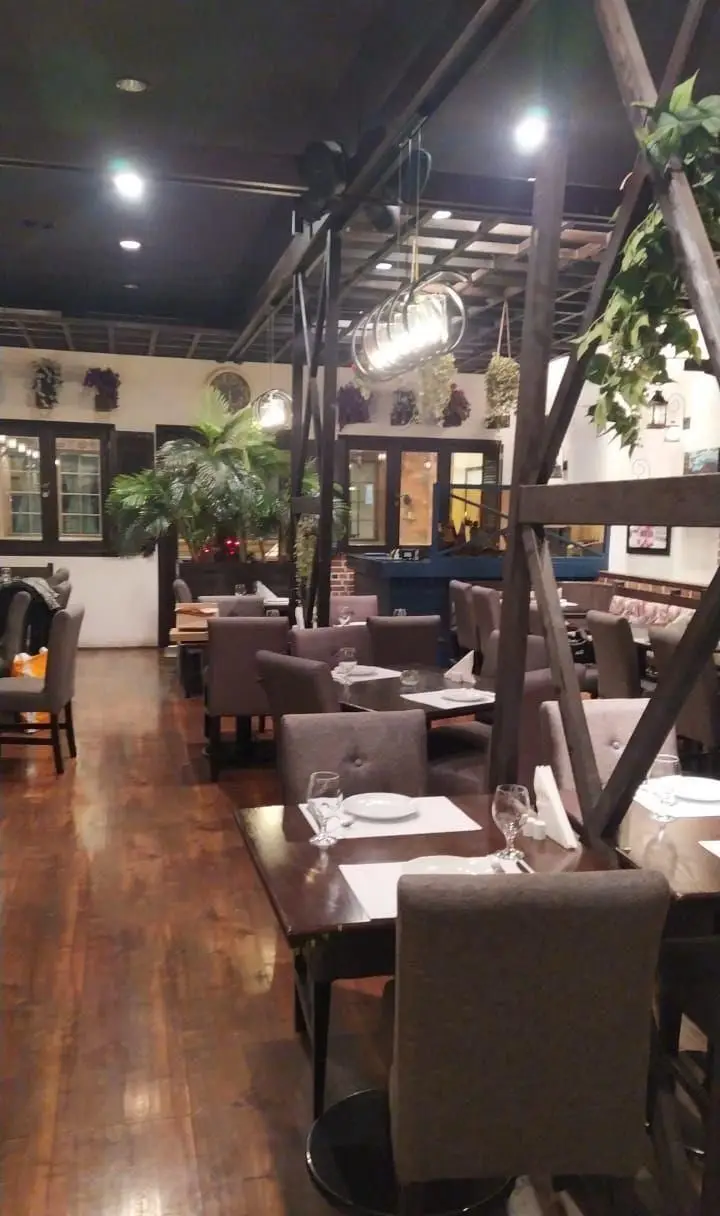 محیط داخلی گرم و دلپذیر رستوران ایتالیایی پارلا با چیدمان میز و صندلی‌های شیک، کفپوش چوبی و دکوراسیون گیاهی چشم‌نواز.