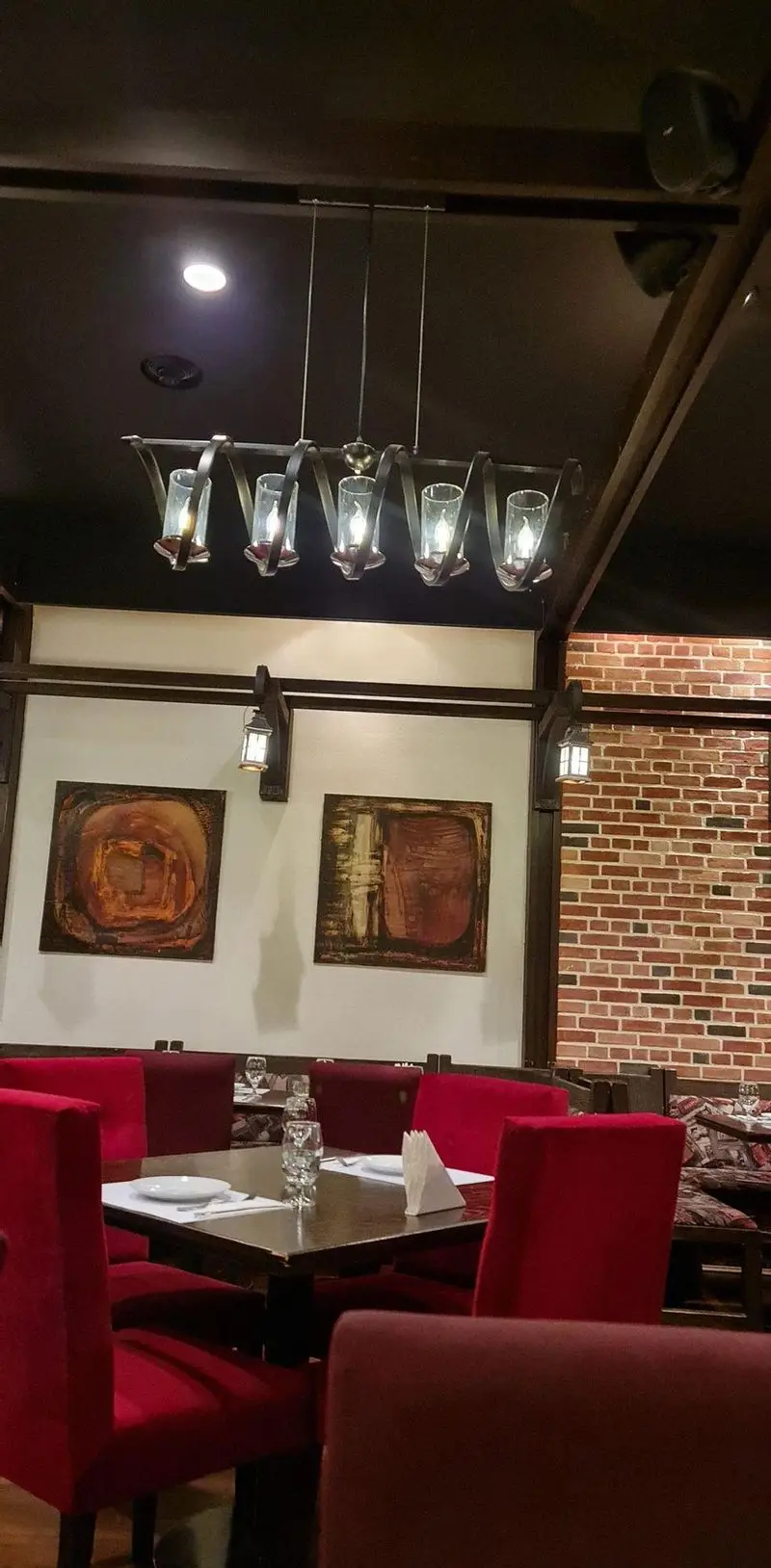 فضای داخلی رستوران ایتالیایی پارلا، با لوستر خاص، صندلی‌های قرمز راحت، و دیوار آجری، محیطی دنج و شیک برای تجربه غذا.