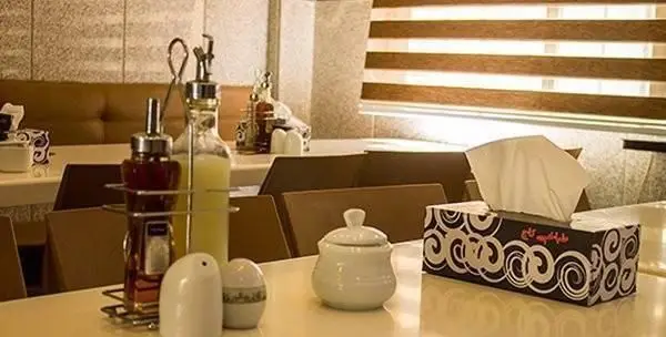 فضای داخلی و میز چیده شده رستوران طباخی کاج سعادت آباد با بطری‌های روغن، سرکه، نمکدان و دستمال کاغذی با لوگوی کاج.