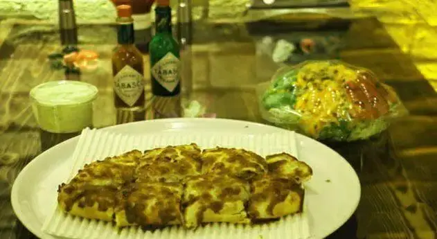 پیتزا یا نان پنیری تازه و خوشمزه از فست فود جاسنتو، همراه با سس تند تاباسکو و سالاد، آماده برای سرو در رستوران.