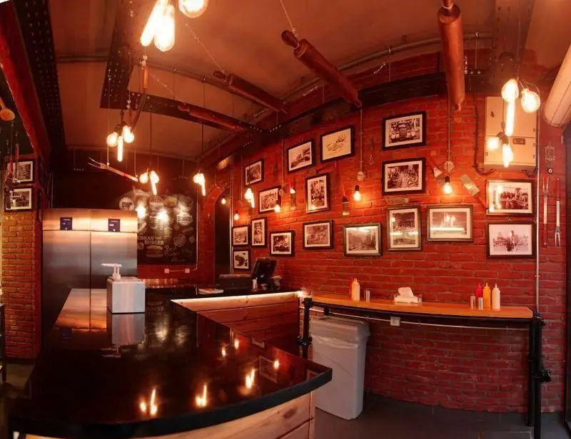 دکوراسیون داخلی چشم‌نواز و صنعتی رستوران تهران برگر، شامل دیوارهای آجری، نورپردازی گرم و تصاویر نوستالژیک.