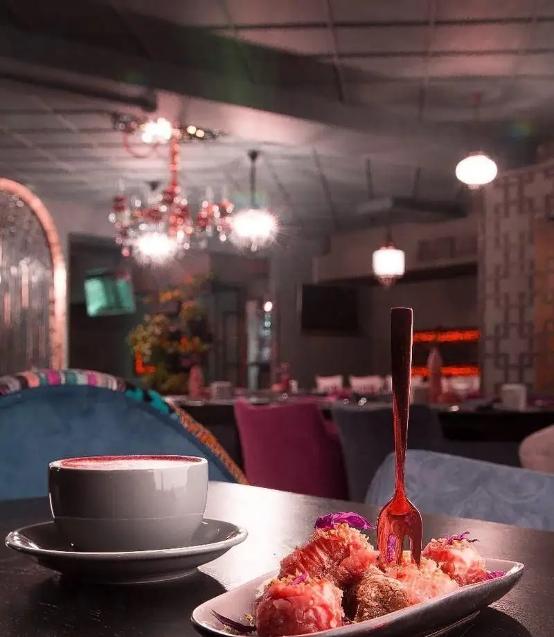 تصویری دلنشین از فضای داخلی کافه رستوران آشا: میز با دسر لذیذ و نوشیدنی گرم، لوسترهای شیک و مبلمان رنگی و راحت