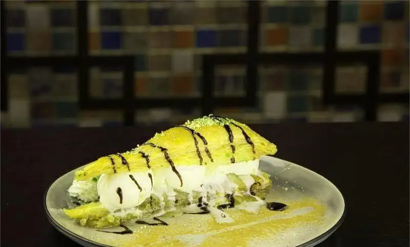 باقلوای پسته ای لذیذ کافه رستوران آشا با بستنی وانیلی، خامه تازه، پودر پسته و سس شکلات. دسری بی‌نظیر برای شما.