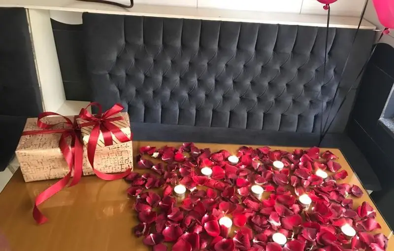 میز آرایی رمانتیک در کافه و سفره خانه دلکده: گلبرگ رز قرمز، شمع و هدایای تولد برای سورپرایز مناسبت خاص در محیطی دلنشین