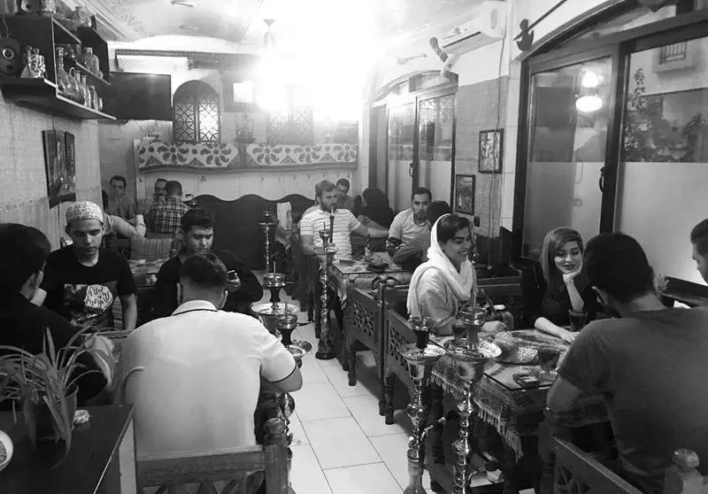 صحنه‌ای پرجنب‌وجوش از مشتریان در کافه و سفره‌خانه دلکده با دکور سنتی، قلیان و فضای صمیمی برای دورهمی‌های دوستانه.