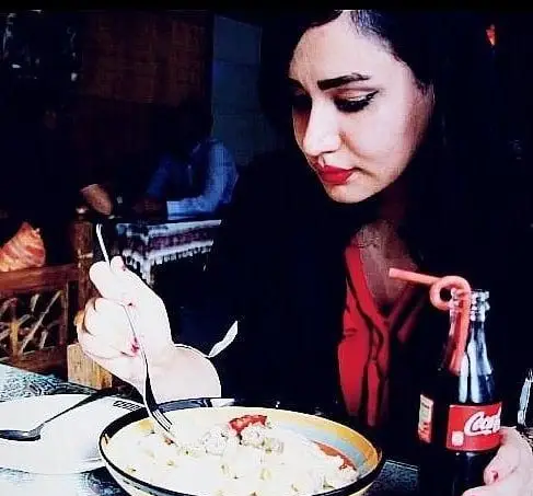 مشتری بانویی در حال میل کردن غذای خوشمزه و کوکاکولا در محیط سنتی و دنج کافه و سفره خانه دلکده.