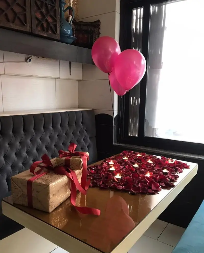 عکس داخلی کافه و سفره خانه دلکده: میز آرایی عاشقانه با شمع، گلبرگ رز، کادو و بادکنک صورتی در محیطی دنج و شیک.