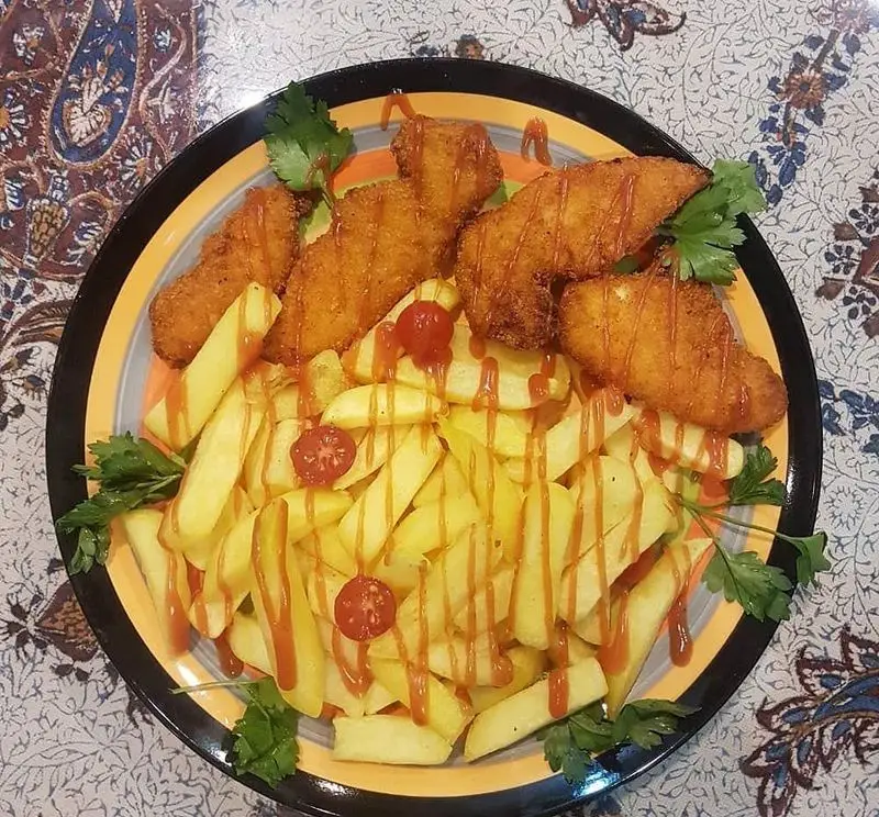بشقاب غذای خوشمزه شامل مرغ سوخاری ترد، سیب زمینی سرخ کرده طلایی با سس کچاپ، مناسب کافه و سفره خانه دلکده.