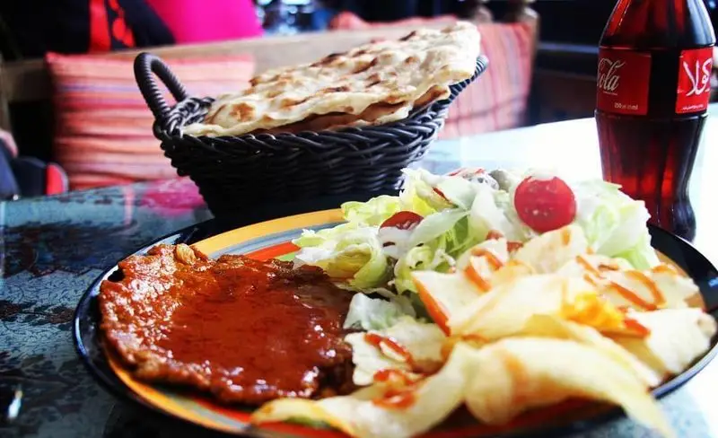 یک وعده غذای کامل و لذیذ در کافه و سفره خانه دلکده شامل خوراک گوشت با سس قرمز، سالاد تازه، چیپس سیب‌زمینی و نان تنوری داغ به همراه نوشابه.