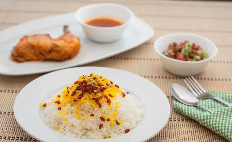 غذای خوشمزه زرشک پلو با مرغ رستوران هانی: برنج زعفرانی، زرشک، ران مرغ، سس و سالاد شیرازی تازه.