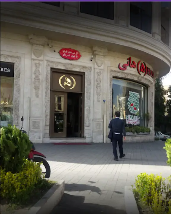 تصویر بیرونی رستوران هانی با معماری کلاسیک و زیبا در تهران. تابلوی شاخص رستوران به همراه محدوده فعالیت آن "از میدان قیام تا بلوار اندرزگو" مشهود است.