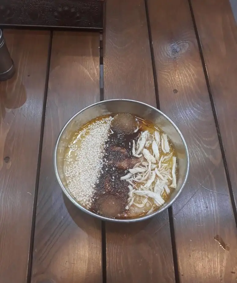 تصویری جذاب از کاسه آش یا حلیم ایرانی با مرغ ریش ریش، کنجد فراوان، کوفته قلقلی و سس مخصوص در کبابسرا و آشکده حاج رضا.