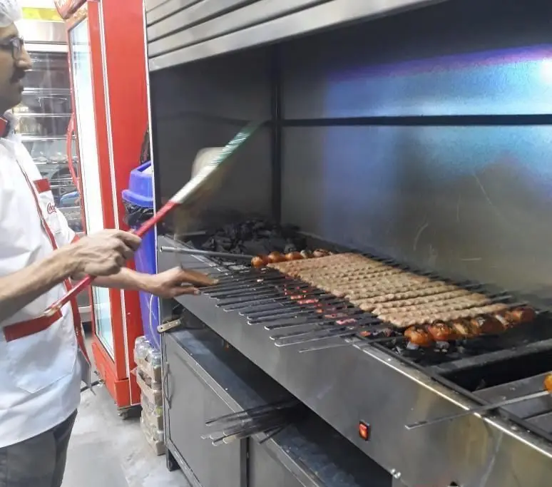 آشپز ماهر کبابسرا و آشکده حاج رضا، کباب کوبیده و گوجه کبابی خوش طعم را روی ذغال آماده می‌کند. لذت غذای ایرانی اصیل.