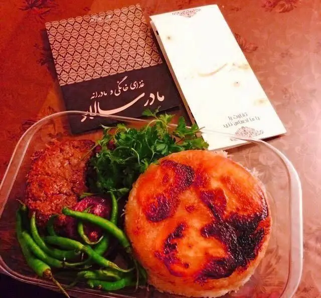 غذای خانگی و مادرانه مادر سالار: یک پرس غذای ایرانی خوشمزه شامل ته دیگ طلایی، کباب، سبزی تازه و فلفل سبز در ظرف بیرون بر، با منو