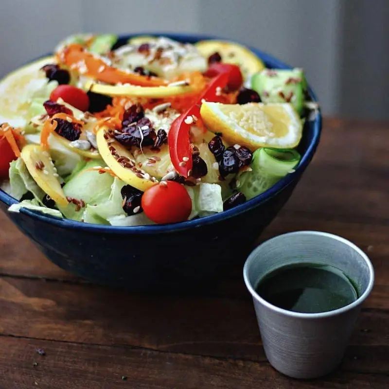 سالاد رژیمی و خوشمزه فرش باکس با سبزیجات تازه، گوجه، کرنبری، دانه های مغذی و برش لیمو، همراه با شات سبز سلامت برای یک وعده سالم و کامل.