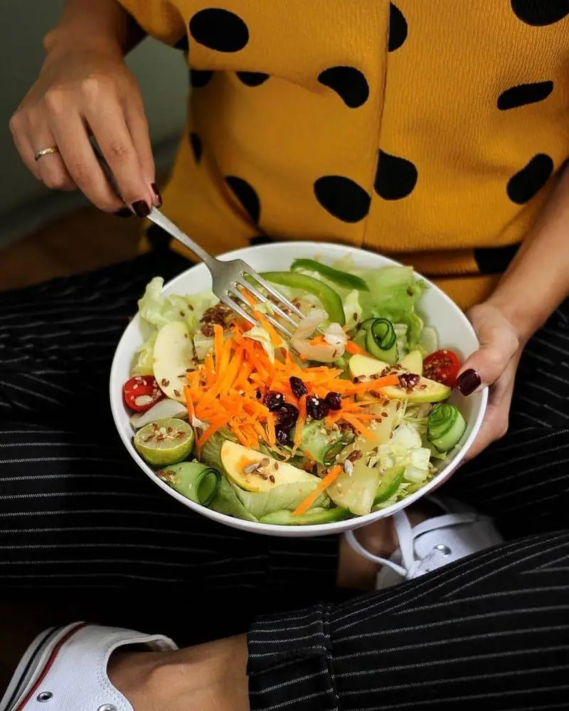 فردی در حال خوردن سالاد بزرگ و رنگارنگ فرش باکس، شامل سبزیجات تازه، میوه‌های سالم و دانه‌های مغذی. غذایی رژیمی و لذت‌بخش.