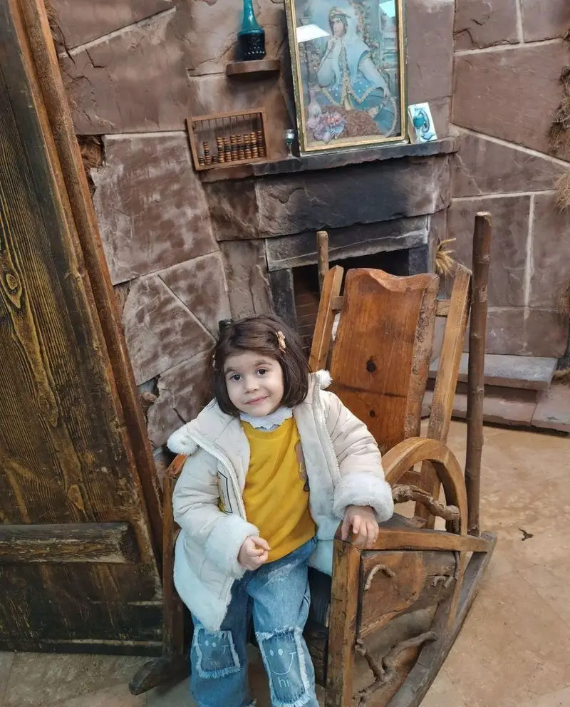 رستوران هودین: دختری خندان نشسته بر صندلی چوبی قدیمی با نقوش سنتی. دکوری گرم و صمیمی برای تجربه غذایی دلپذیر در محیط خانوادگی.