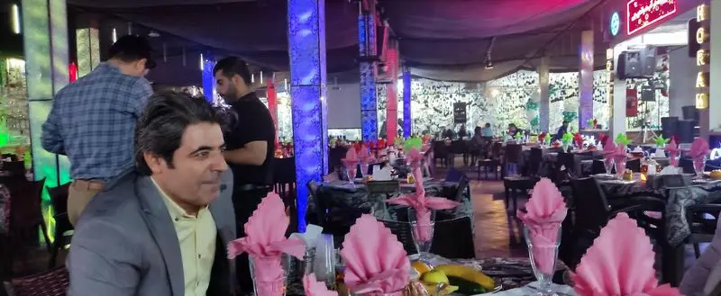 رستوران هودین: محیطی دلنشین و مدرن با نورپردازی رنگارنگ، میزهای چیده شده برای شام، و مهمانان در حال لذت بردن از فضای خاص.