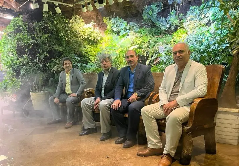 چهار مرد در رستوران هودین با دکوراسیون داخلی چشم‌نواز شامل دیوار سبز گیاهی و مه ملایم، در محیطی آرامبخش.