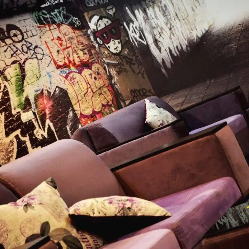 دکوراسیون داخلی منحصر به فرد کافه دلفین با مبلمان راحتی مخملی بنفش و دیوارنگاره‌های چشم‌نواز شهری، فضایی خاص و دلنشین.