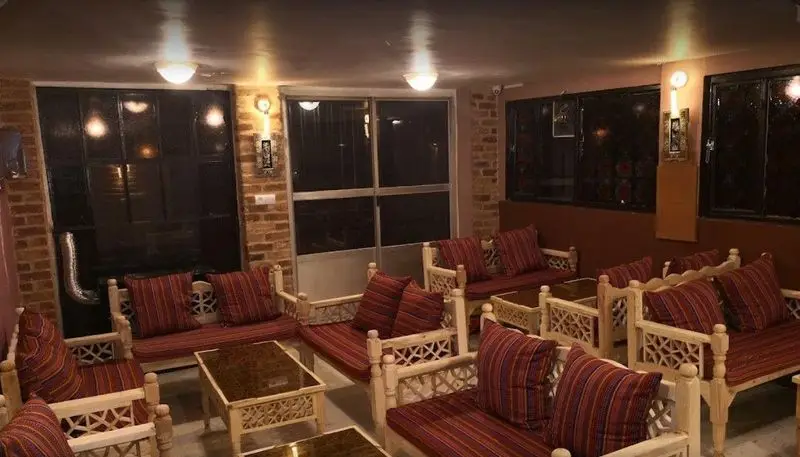 تصویری از داخل کافه سنتی ترنه با دکوراسیون دنج ایرانی، نیمکت‌های چوبی سنتی، کوسن‌های قرمز و میزهای منبت‌کاری شده.