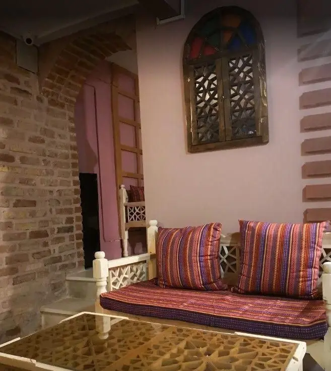 فضای داخلی کافه سنتی ترنه با مبلمان چوبی، کوسن‌های رنگی و میز سنتی، معماری آجری و پنجره دکوراتیو. محیطی دلنشین برای مشتریان.