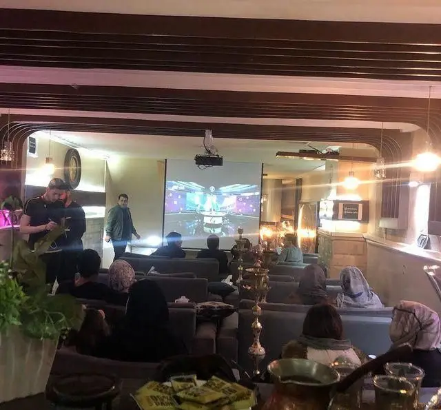 فضای داخلی کافه سفره خانه رز سیاه؛ مهمانان در حال تماشای برنامه از طریق پروژکتور، لذت بردن از قلیان و دورهمی دوستانه.