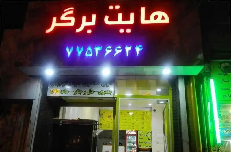 نمای بیرونی فست فود هایت برگر در شب با تابلوی نئون قرمز هایت برگر و شماره ۷۷۵۳۶۶۲۴. ارائه انواع ساندویچ، بندری، دل و جگر و هات داگ.