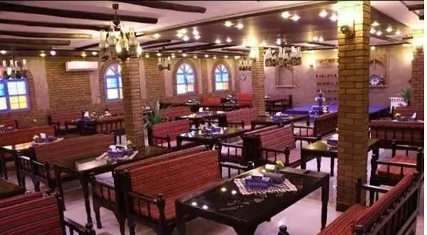 نمای داخلی رستوران ایرانی کاه گل با دکوراسیون سنتی، دیوارهای آجری، پنجره‌های رنگی و میز و صندلی‌های چوبی آماده پذیرایی