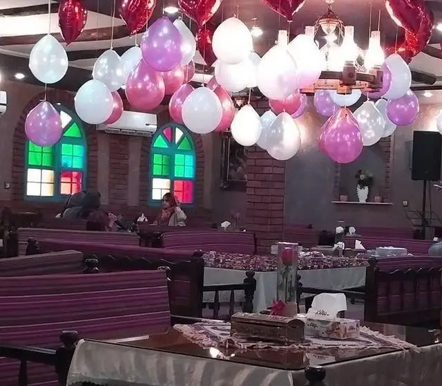 رستوران ایرانی کاه گل با دکوراسیون جشن و بادکنک‌های زیبا، پنجره‌های رنگی، تخت‌های سنتی و فضای گرم و دلنشین آماده پذیرایی مهمانان.