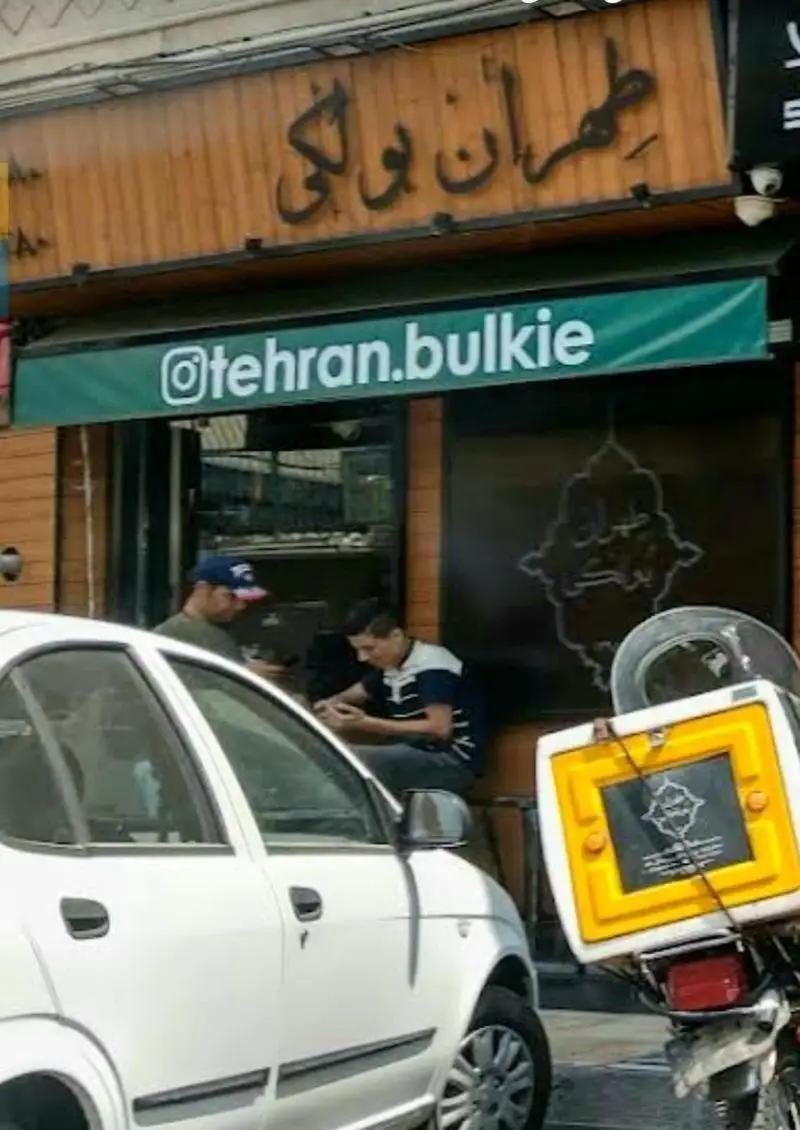 نمای بیرونی طهران بولکی در تهران با مشتریان، خودرو و موتورسیکلت تحویل غذا. حساب اینستاگرام: @tehran.bulkie. ارائه ساندویچ‌های بولکی.
