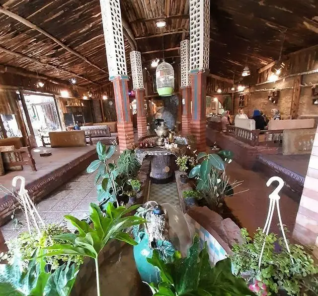 فضای داخلی آرامش‌بخش و سنتی باغ رستوران سفره ایرانی با سقف چوبی، گلدان‌های طبیعی، جوی آب و نشیمن‌های دلنشین.