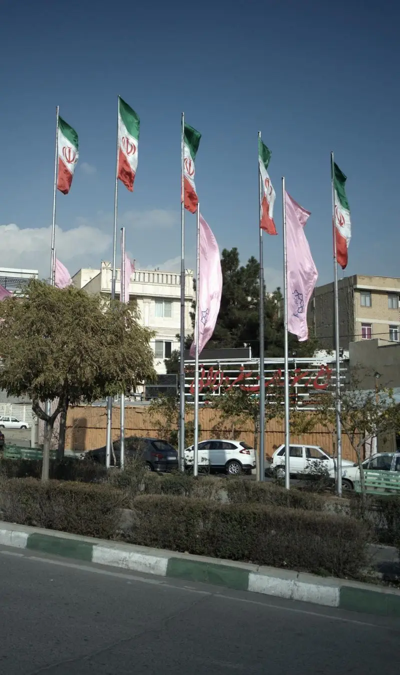 ورودی دلنشین باغ رستوران سفره ایرانی با پرچم‌های ایران و فضایی سرسبز، مکانی ایده‌آل برای تجربه غذای اصیل ایرانی در تهران