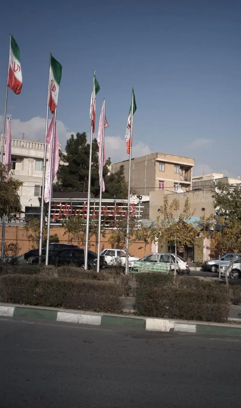 نمای بیرونی باغ رستوران سفره ایرانی در روزی آفتابی، با پرچم‌های سه رنگ ایران و فضای سرسبز. محیطی دلنشین برای غذای اصیل ایرانی.